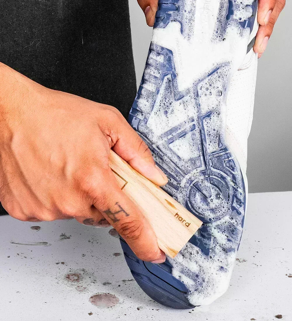 Person cleaning a blue and white sneaker outsole with the SHOEGR Hard Shoe Brush