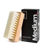 SHOEGR Medium brush with wooden handle and white PP bristles next to its packaging on a white background